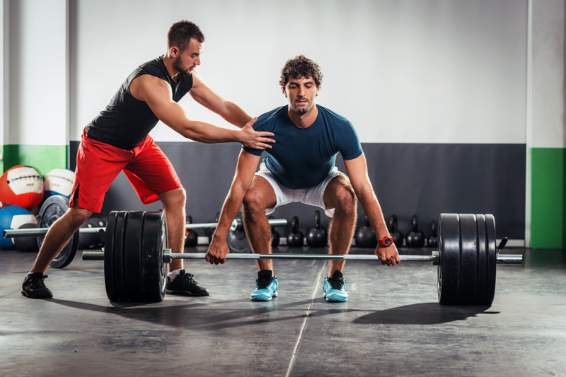 trainer helping man with deadlifting